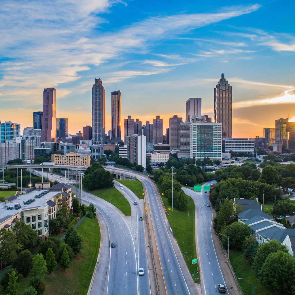 A breathtaking view of the Atlanta, Georgia skyline at sunset, featuring modern skyscrapers, winding highways, and lush greenery. Transportvibe