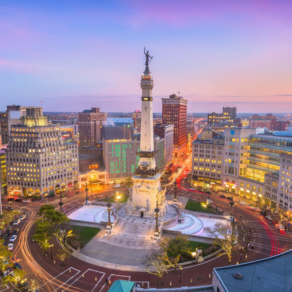 A beautiful evening view of Monument Circle in downtown Indianapolis, Indiana, featuring the Soldiers and Sailors Monument surrounded by illuminated city buildings. indiana | Transportvibe