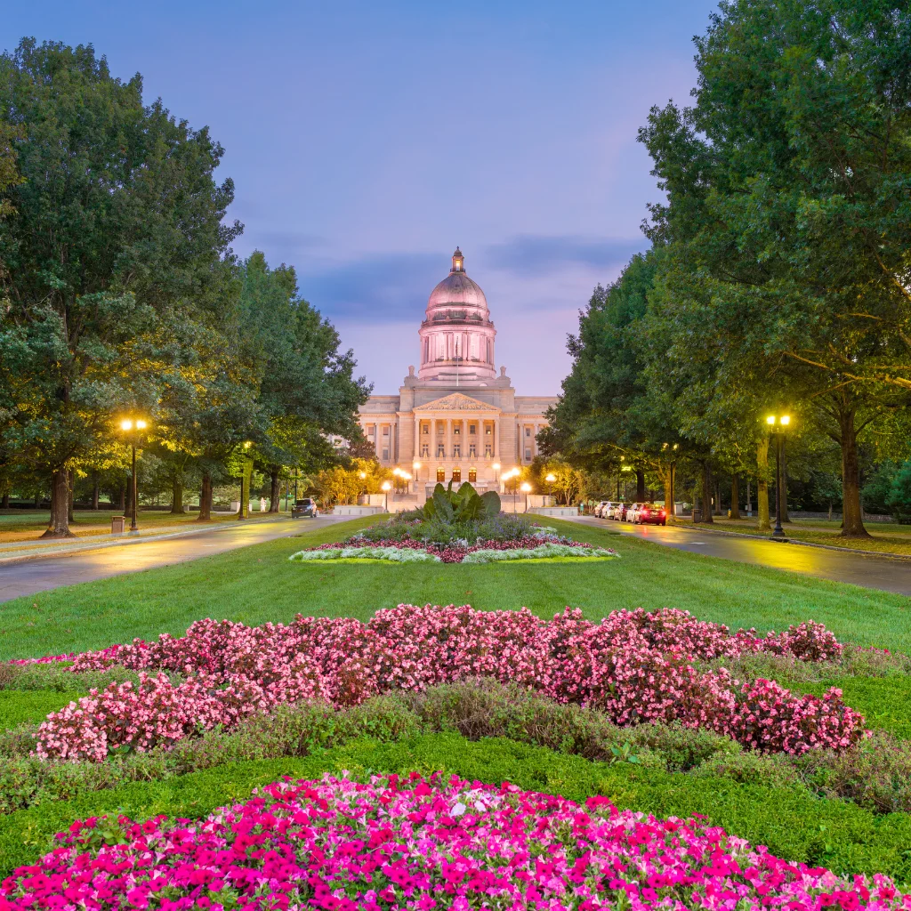 Kentucky State Capitol in Frankfort, surrounded by gardens and evening lights. Transportvibe