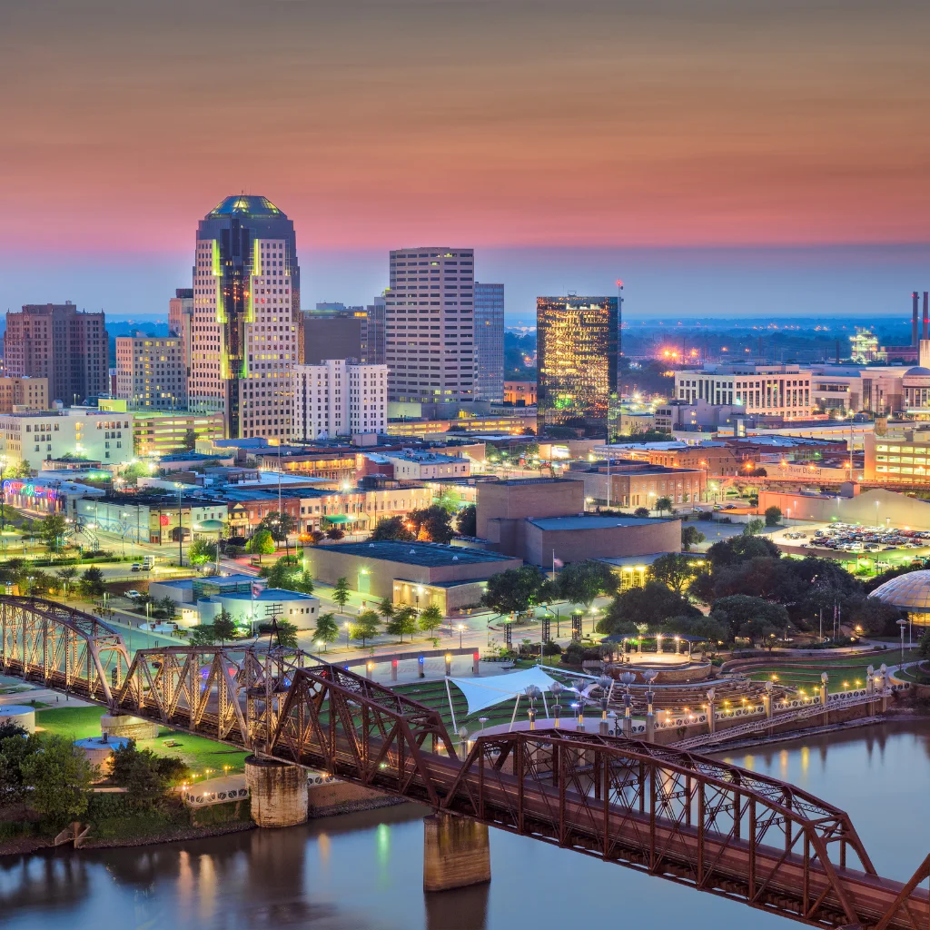 Shreveport, Louisiana skyline at dusk with city lights and a river bridge. Transportvibe