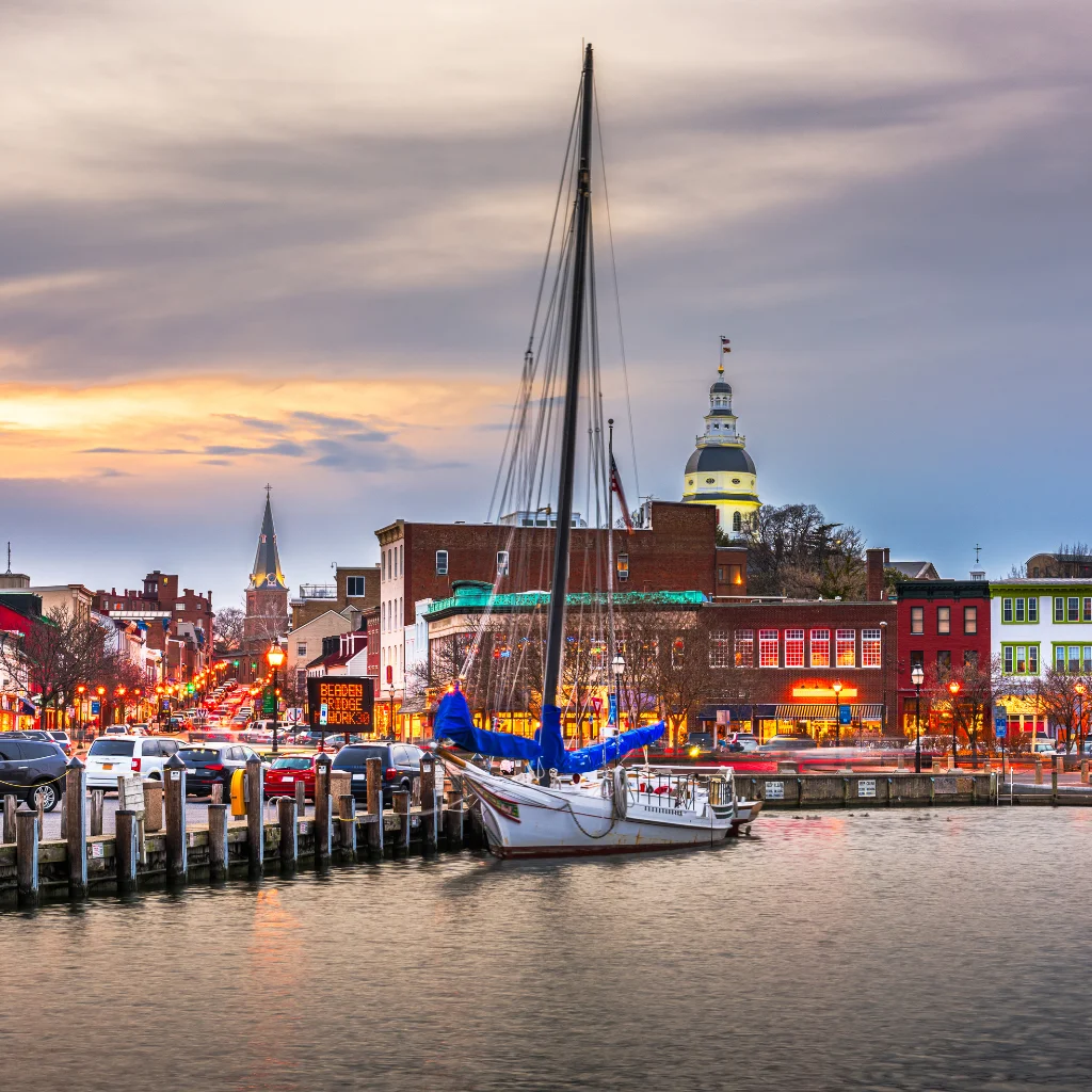 Annapolis Harbor in Maryland at sunset with a sailboat and historic buildings. Transportvibe