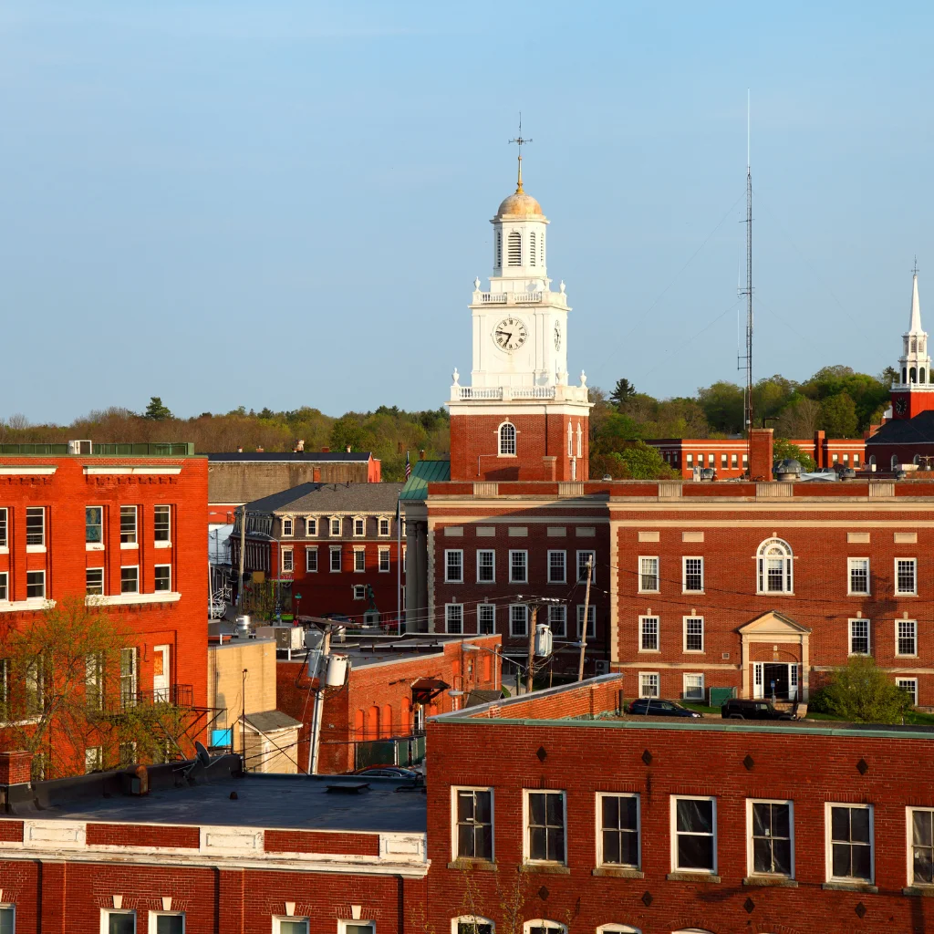 A historic town hall with a clock tower in New Hampshire, surrounded by red brick buildings. Transportvibe