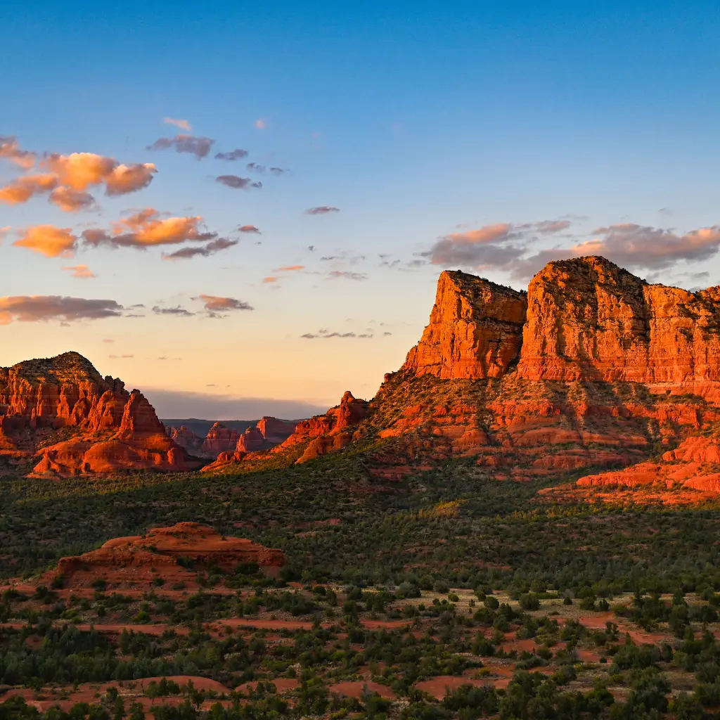 A stunning view of Arizona's red rock formations at sunset, with rugged cliffs illuminated by golden light and a vast desert landscape stretching beyond. Transportvibe