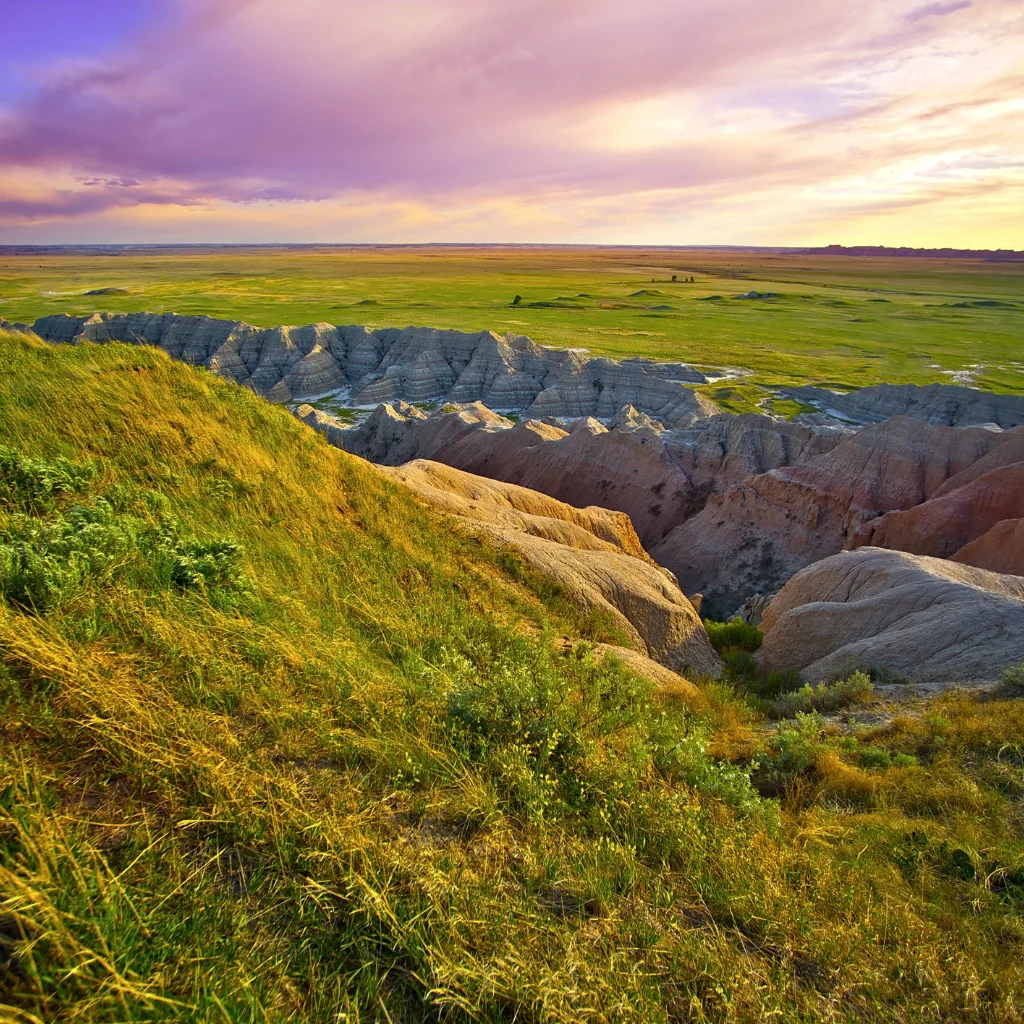The Badlands of South Dakota at sunset with rolling grasslands and rugged rock formations. Transportvibe
