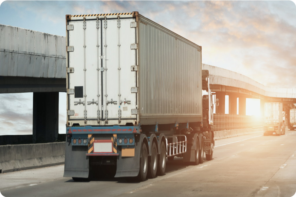 A row of white semi trucks parked along a winding road in a scenic forested area during golden hour.Enclosed Vehicle Shipping . USA . Transportvibe 1