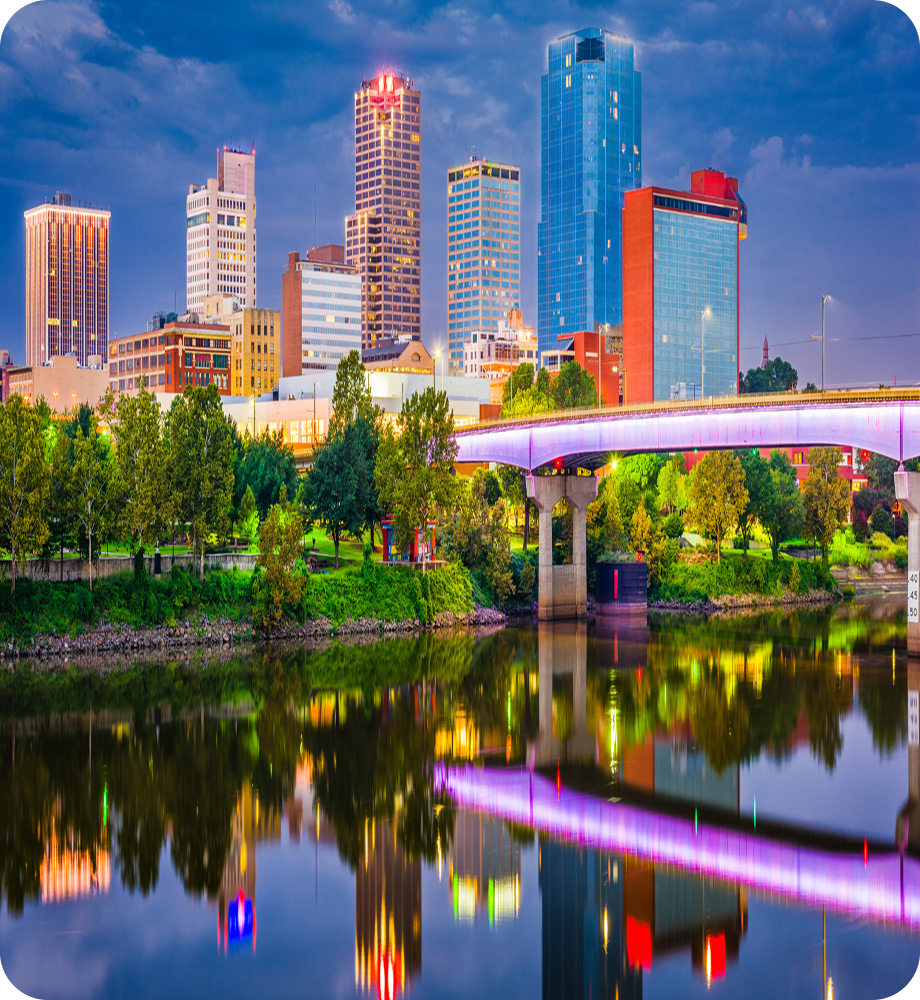 A vibrant view of the Little Rock Arkansas skyline at sunset featuring a colorful sky illuminated bridge and reflections on the Arkansas River. Transportvibe